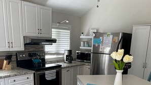 A modern kitchen with white cabinets, stainless steel appliances, a dining table with chairs, and a vase with flowers. - Woodland Beach House in lovely Tiny Beaches! (Elmvale)