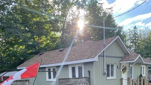 A single-story house with a sloped roof, a wooden fence, and a small garden area with flowers. - Woodland Beach House in lovely Tiny Beaches! (Elmvale)