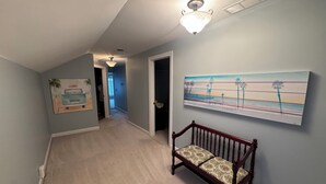 Un couloir avec un banc, un luminaire au plafond et un tableau sur le mur représentant un paysage de plage.