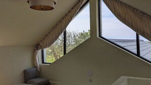 A bedroom with a sloped ceiling, a large window, a bed, a chair, and a small table. - The Rookery (Tacumshane)