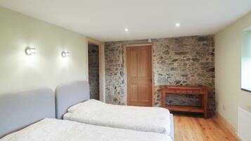 Une pièce avec deux lits, un mur en pierre, une porte en bois et une petite armoire en bois.