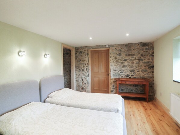 A room with two beds, a stone wall, a wooden door, and a small wooden cabinet. - The Rookery (Tacumshane)