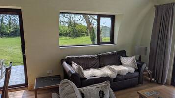 Ein Wohnzimmer mit einer Ledersofa, einem kleinen Tisch, einer Lampe und einem Fenster mit Blick auf einen Garten.