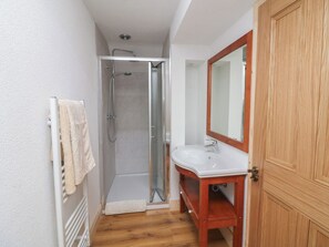 A bathroom with a glass shower enclosure, a white sink with a wooden vanity, and a wooden door. - The Rookery (Tacumshane)