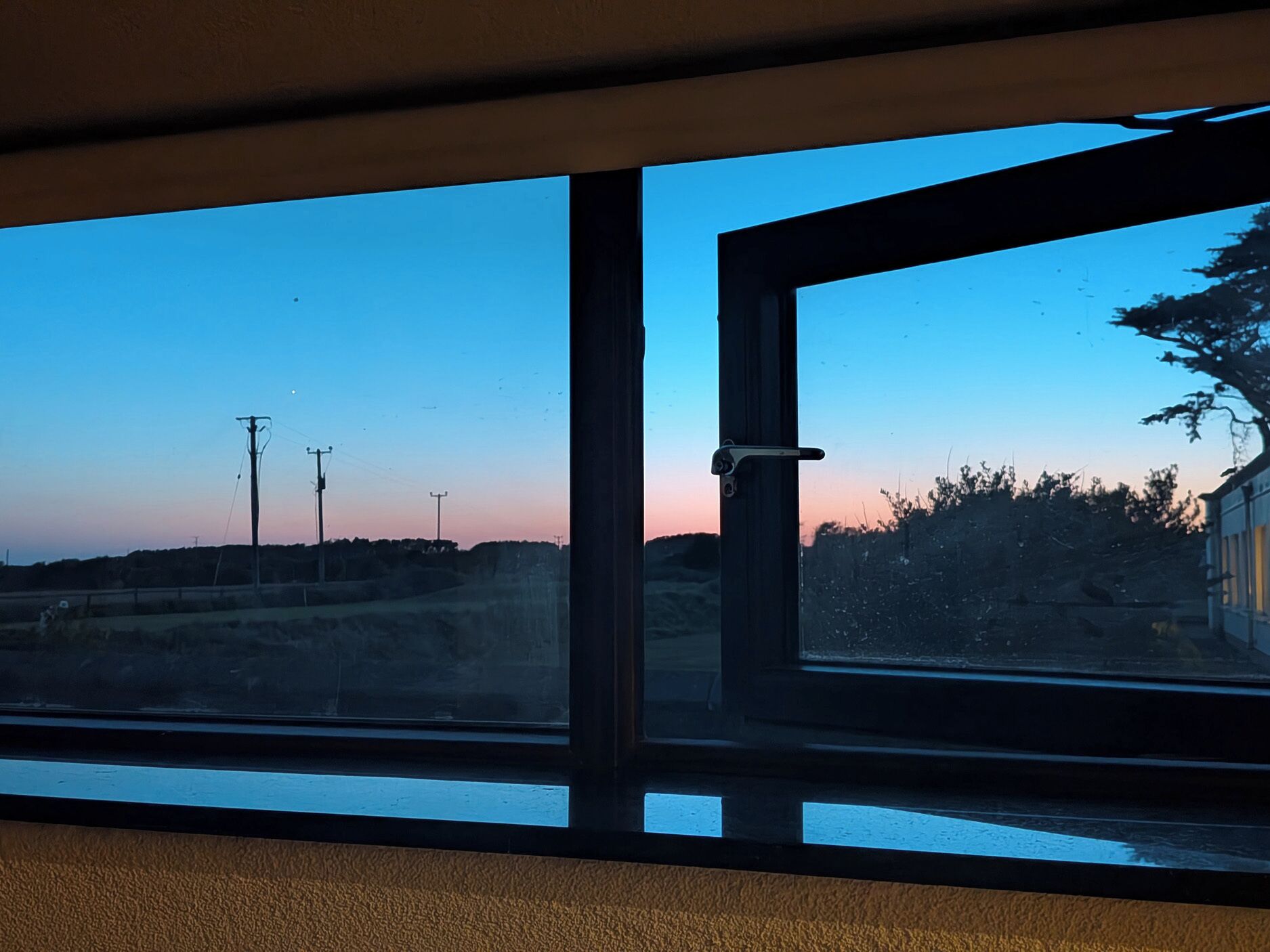 Ein Zimmer mit großem Fenster und Blick auf eine Landschaft mit Bäumen und Stromleitungen.