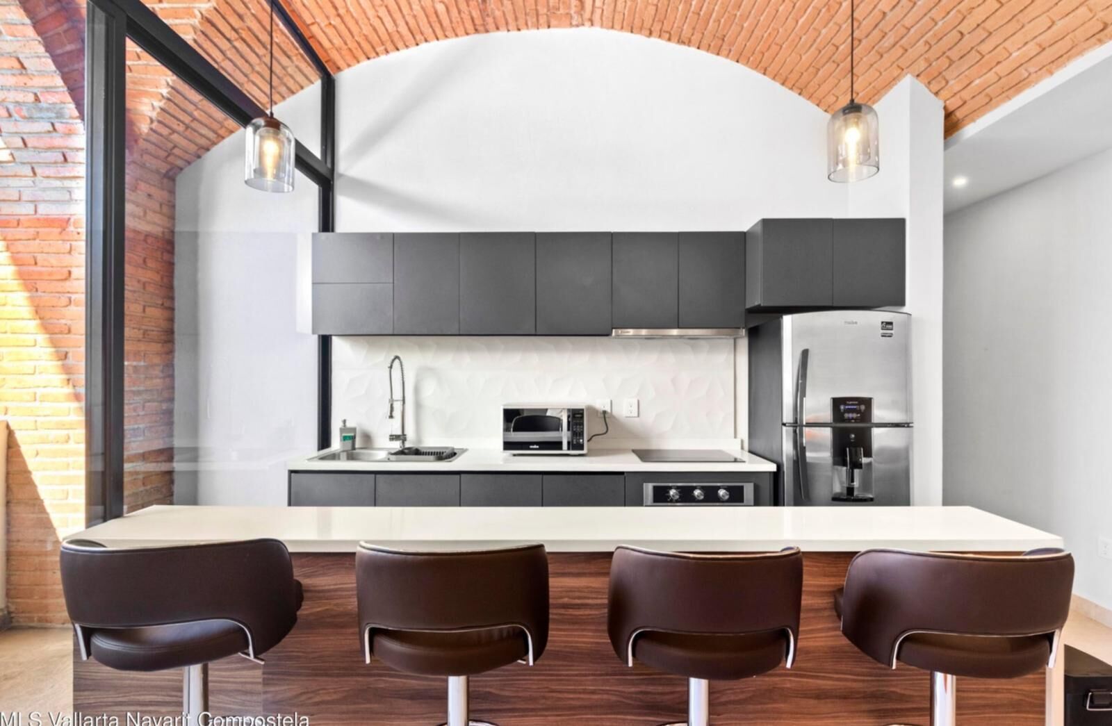 A modern kitchen with a central island, dark cabinets, and stainless steel appliances.