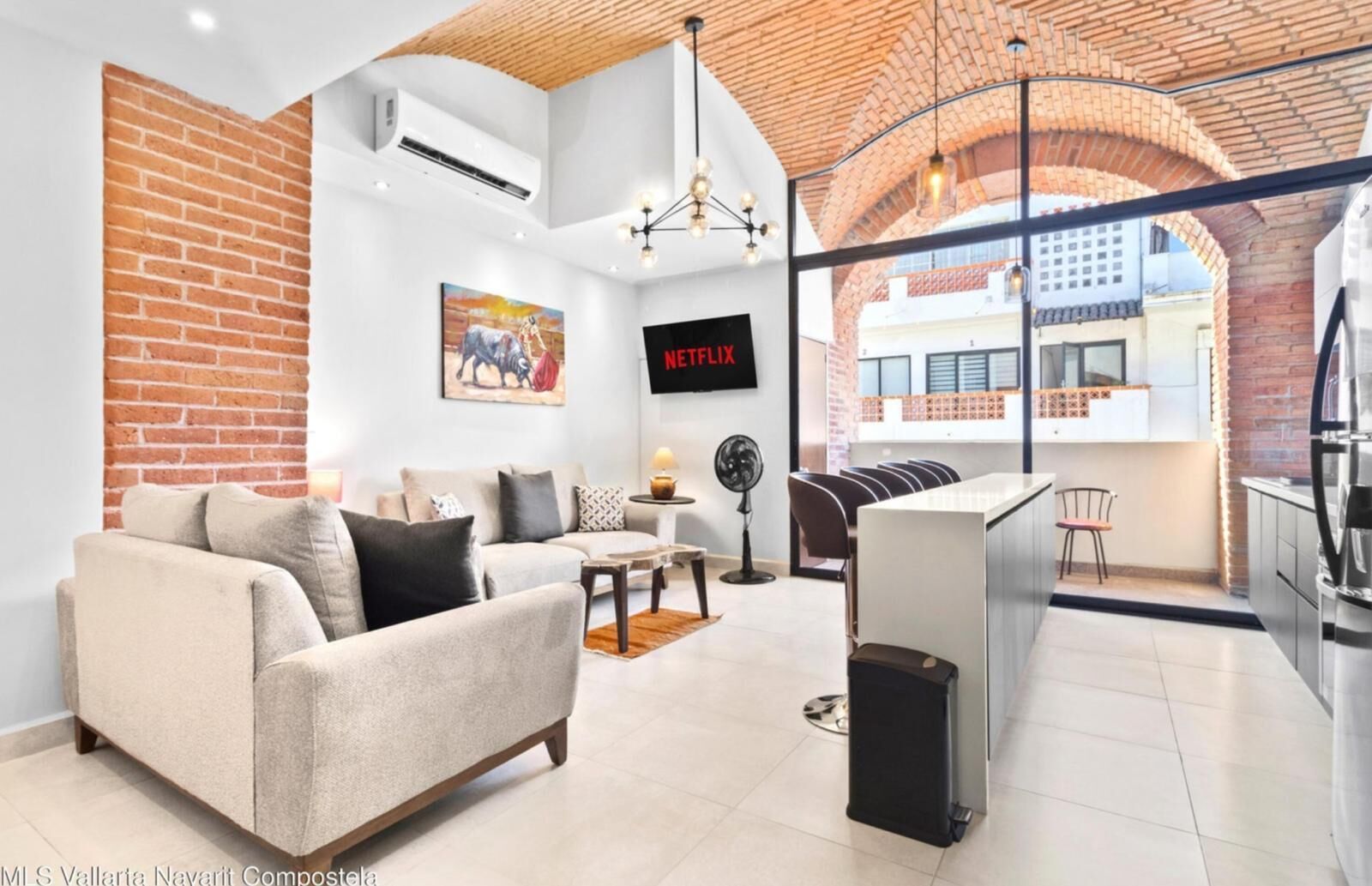 A modern living room with a sofa, a TV, and a kitchen area with a refrigerator.