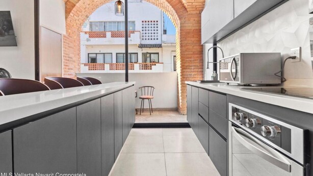 A modern kitchen with a central island, stainless steel appliances, and a view through an arched window to an outdoor balcony. - Perfect 2-bedroom condo Casa Arte with AC in Puerto Vallarta (Puerto Vallarta)