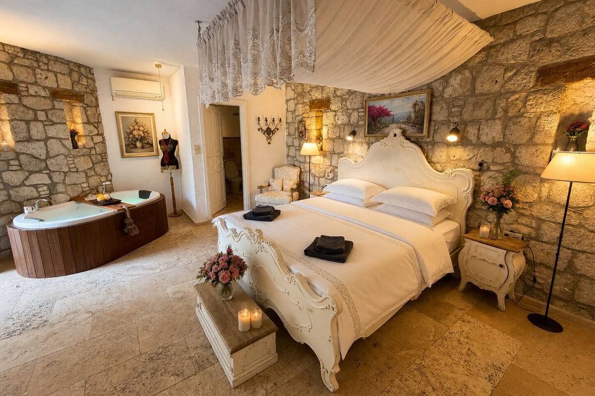 Un dormitorio con pared de piedra, una cama grande con ropa blanca, una bañera y un tocador con espejo.