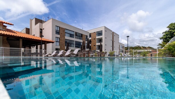 Et moderne hotel med swimmingpool, liggestole og et overdækket område med parasoller.
