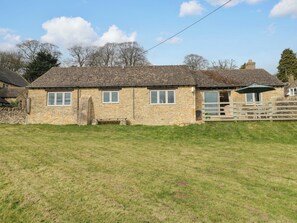 A stone cottage with a tiled roof, a small porch with a bench, and a grassy yard.
