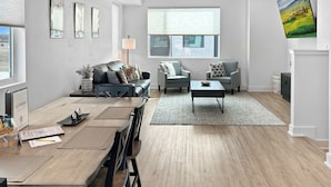 A modern living room with a dining area, featuring a sofa, armchairs, a coffee table, and a dining table with chairs.