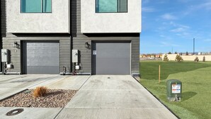 A modern two-story building with a garage door, a landscaped front yard with a small garden bed, and a mailbox.