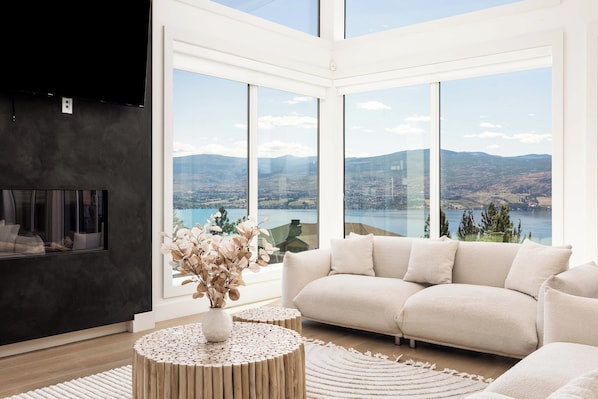 A modern living room with a large window offering a scenic view of mountains and a lake.