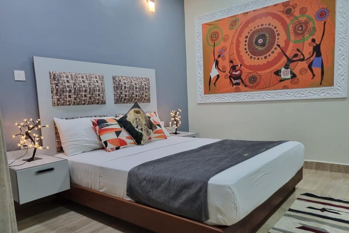 A bedroom with a bed, nightstands, a wall-mounted artwork, and a patterned rug.