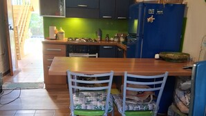 A kitchen with a wooden table and two chairs, a refrigerator, and cabinets. - Beachfront with pool Eucalyptus garden (Alghero)