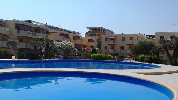 A swimming pool area with tiled flooring and a clear blue pool. - Beachfront with pool Eucalyptus garden (Alghero)