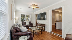 A living room with a brown leather sofa, a glass coffee table, a ceiling fan, and a flat-screen TV. - Camp Carolina 3BR 2BA home with private pool close to beach! (Isle Of Palms)