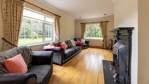A spacious living room with two sofas, a fireplace, and large windows offering a view of greenery.