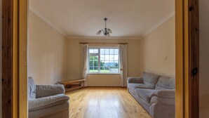 A spacious room with a wooden floor, two sofas, a bench, and a window with curtains.