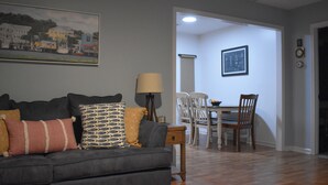Una sala de estar con un sofá, una mesa de comedor con sillas, una lámpara y un cuadro en la pared.