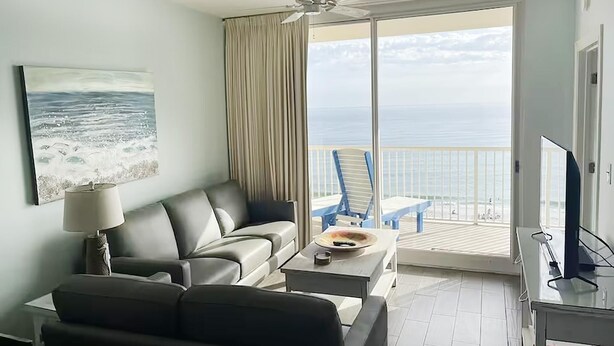 A hotel room with a balcony, a sofa, a table, and a TV. - Majestic Beach Towers 2-305 (Panama City Beach)