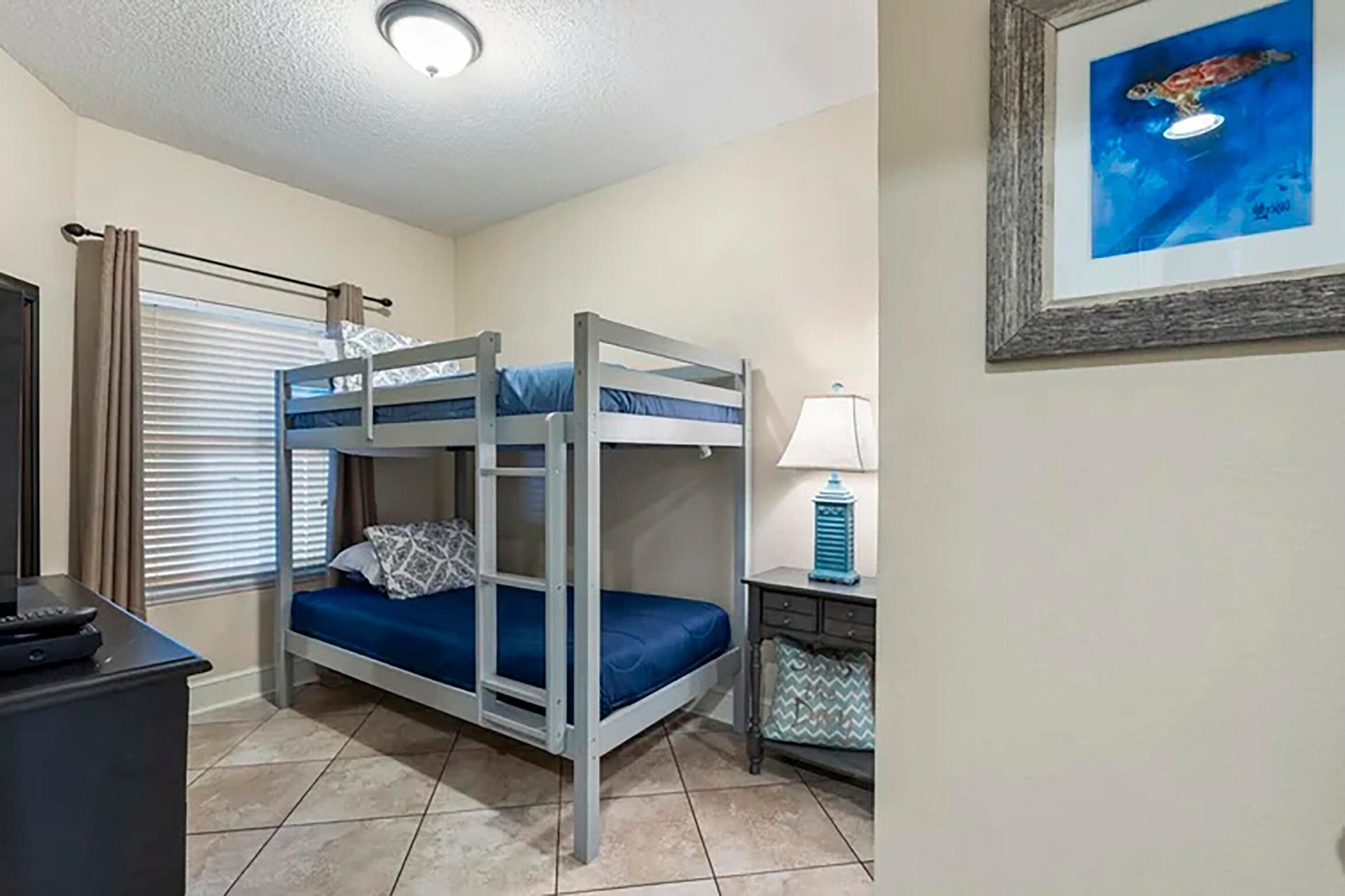 A bunk bed room with a desk, lamp, and framed picture on the wall.