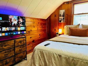 Ein Hotelzimmer mit Holzwand, Flachbildfernseher, Bett mit weißer Bettwäsche und Nachttisch mit Lampe.