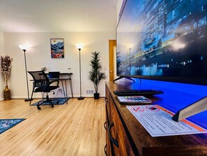 Ein moderner Arbeitsplatz mit Schreibtisch, Stuhl, Computer und einem großen Bildschirm, der eine Stadtansicht zeigt.