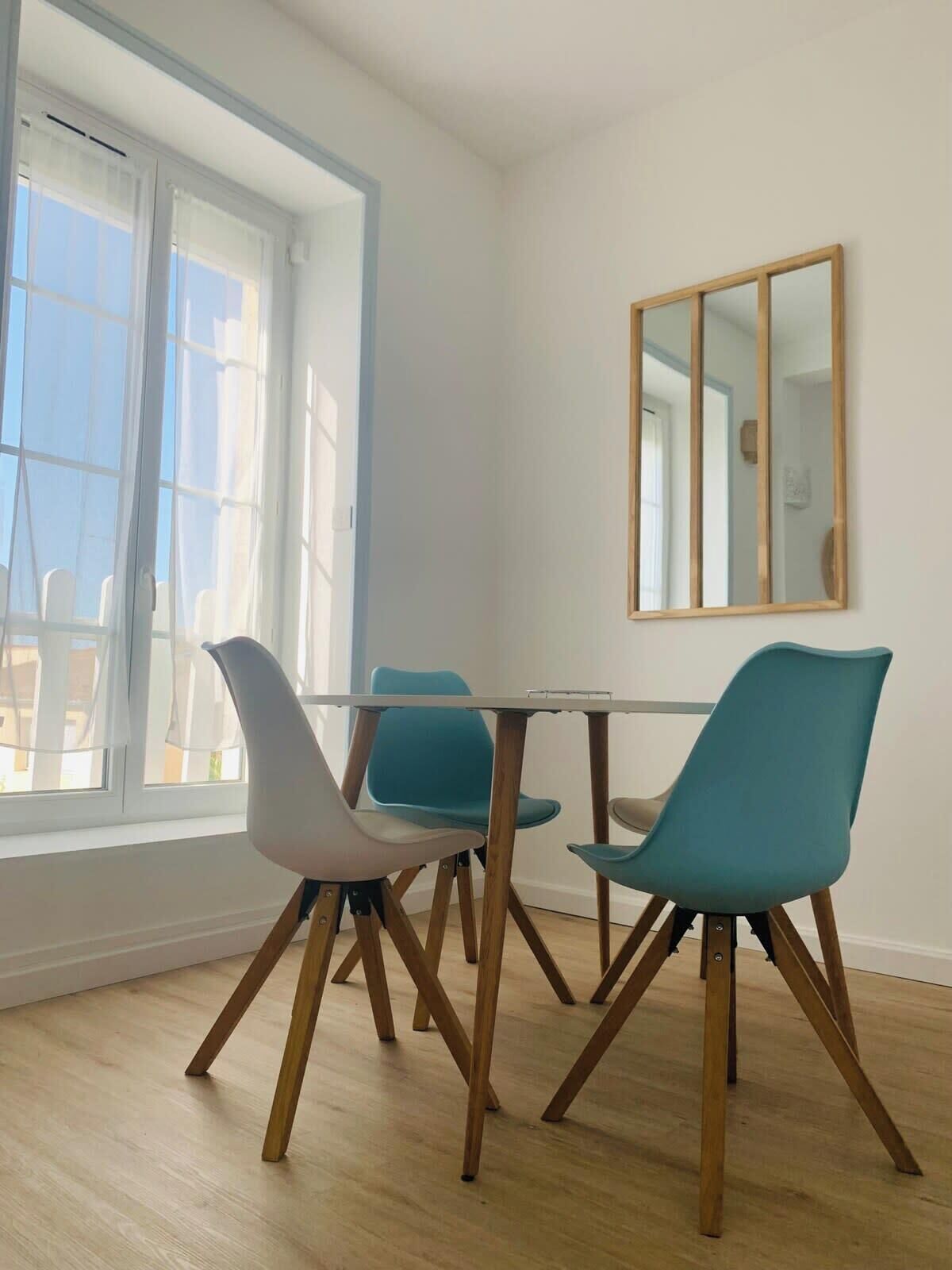 A dining area with a table and four chairs, large windows, and a mirror on the wall.