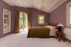 A bedroom with a bed, a window, a shelf with books, and a lamp.