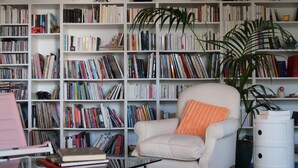 Una stanza con una poltrona bianca, un tavolino in vetro e una libreria piena di libri.