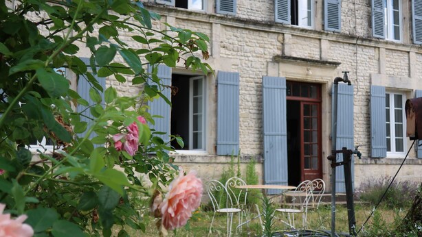 Un edificio in pietra con persiane blu, un giardino con rose e posti a sedere all'aperto.