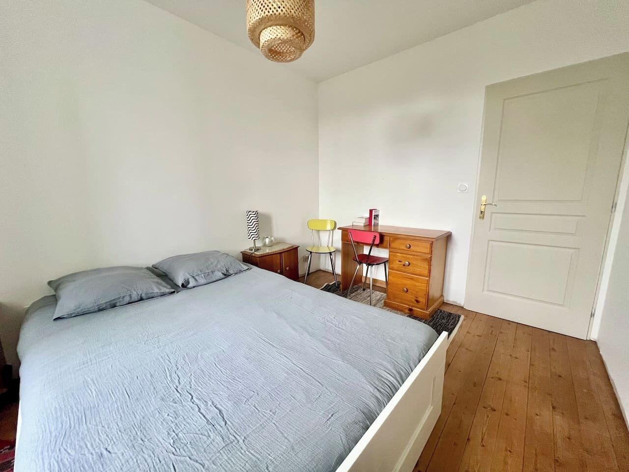 A bedroom with a bed, a dresser, a chair, a lamp, and a door.