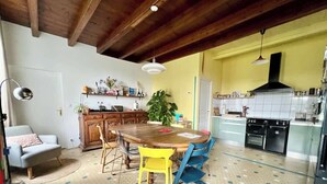 Zona pranzo con tavolo e sedie in legno, cucina con mobili bianchi e piano cottura nero, e parete gialla.