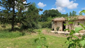 Un edificio rustico in pietra con tetto di paglia, circondato da vegetazione lussureggiante e alberi.