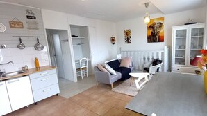 A modern kitchen with white cabinets, a dining area with a grey sofa, and a yellow vase with flowers.