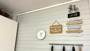 A kitchen with white cabinets, a clock, and hanging pots. There are signs with French phrases and a bicycle decoration.