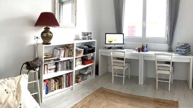 A study room with a desk, computer, chair, bookshelf, lamp, and a window with curtains.