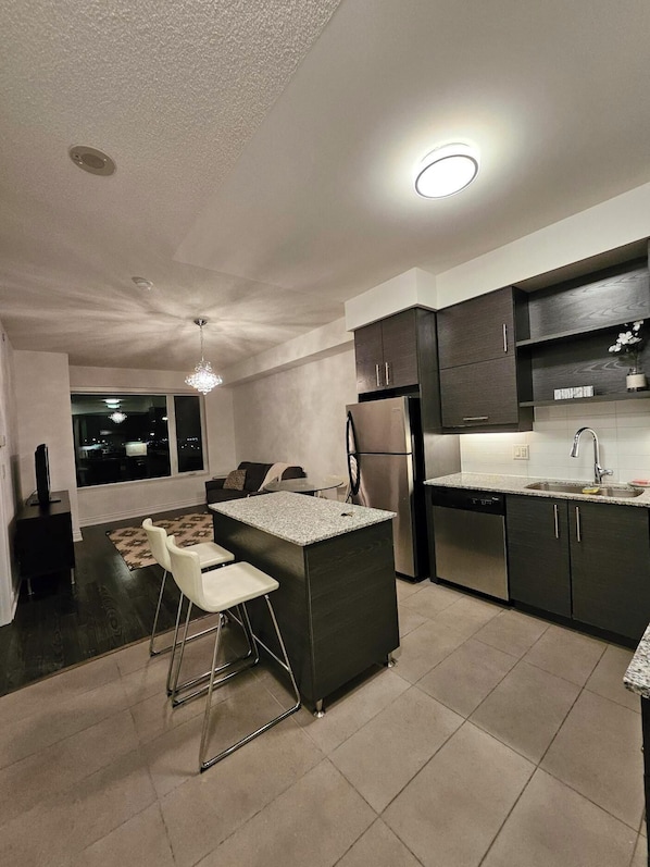 A modern kitchen with a central island, dark cabinetry, and a built-in dishwasher.