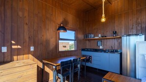 A compact kitchen with wooden walls, a window, a hanging light fixture, a built-in oven, and a refrigerator. - Romantic Cabin With Amazing View Vst002 (Anitapolis)