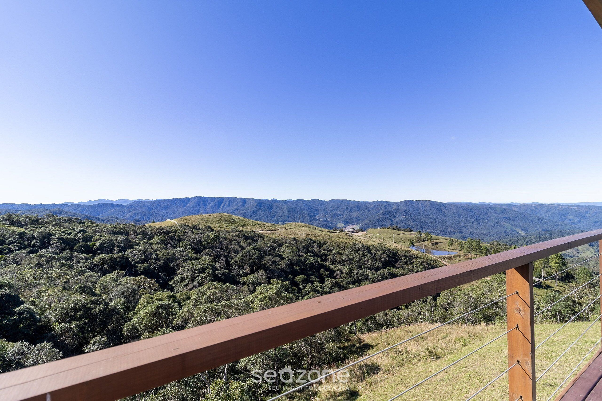 Vista panorámica desde un balcón de madera con vistas a un valle exuberante y colinas lejanas.