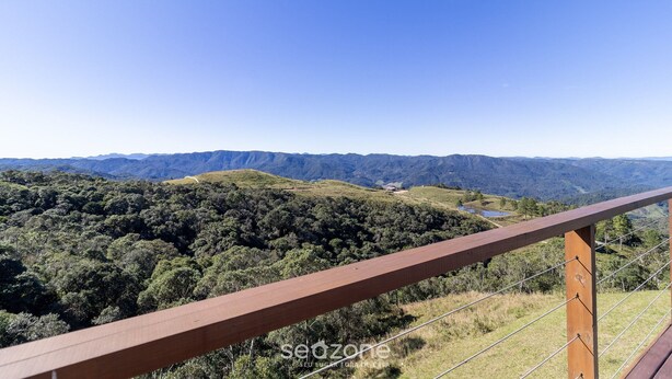 Vista panorámica desde un balcón de madera con vistas a un valle exuberante y colinas lejanas.