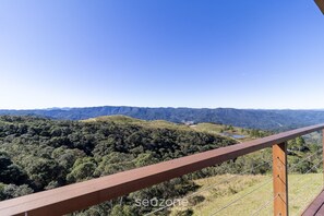 Vista panorámica desde un balcón de madera con vistas a un valle exuberante y colinas lejanas.