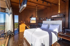Ein Schlafzimmer mit einem großen Bett, Holzboden und Blick durch eine Glastür.
