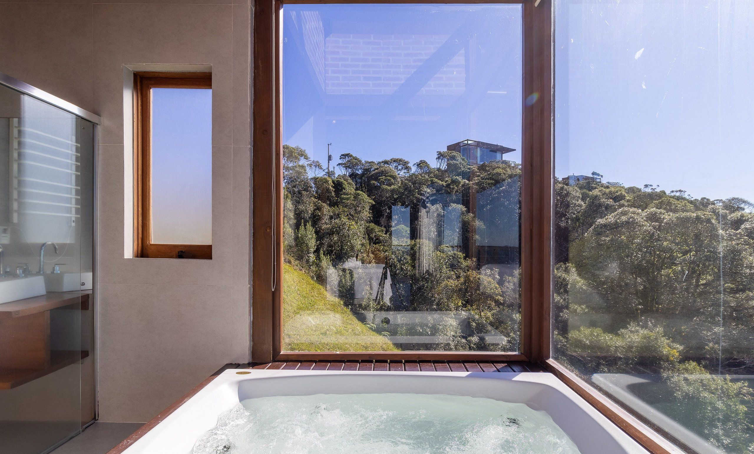A modern bathroom with a large window, a bathtub, and a mirror.