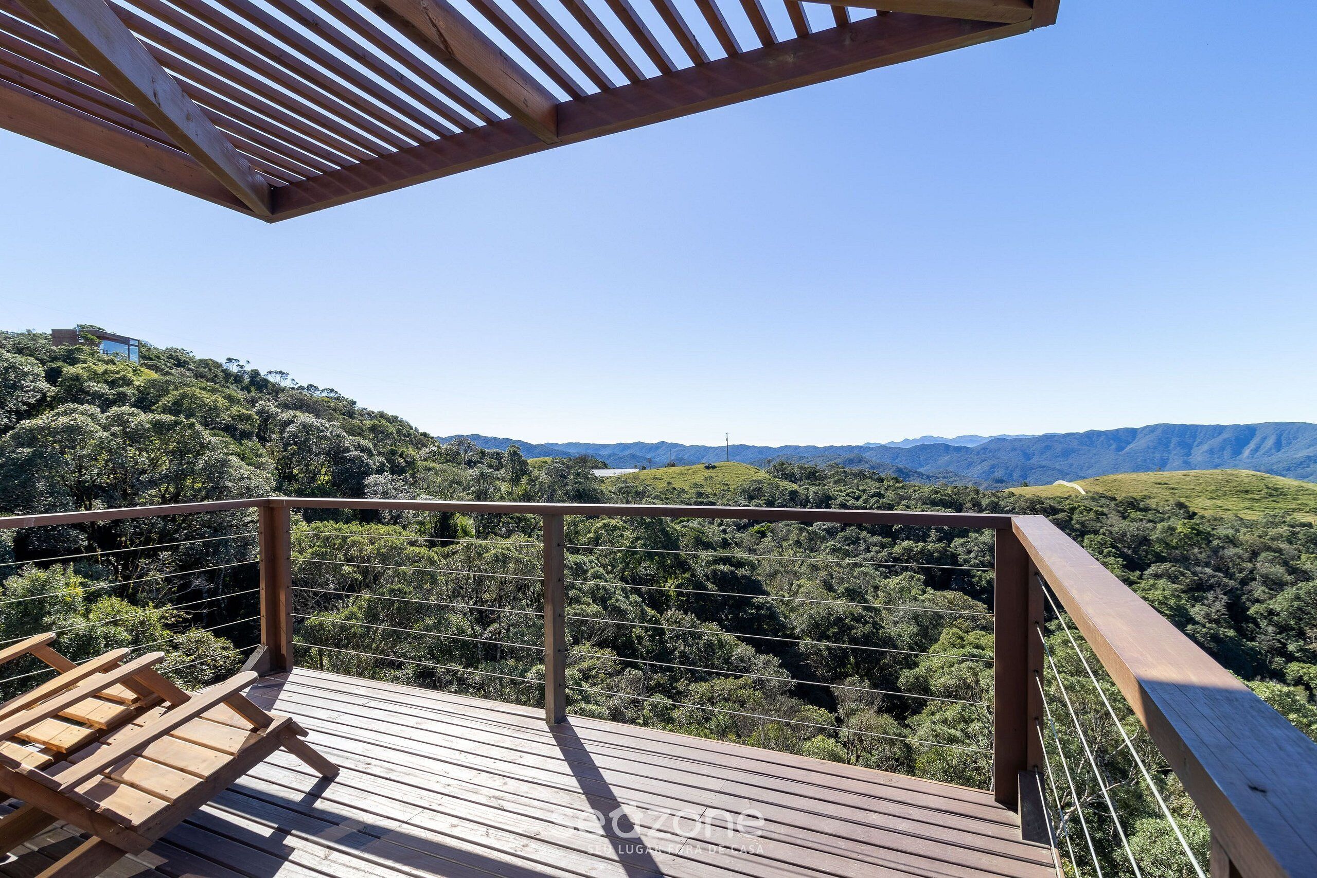Um deck de madeira com guarda-corpo, com vista para um morro coberto de árvores.