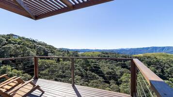 Um deck de madeira com guarda-corpo, com vista para um morro coberto de árvores.