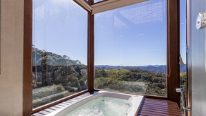 Un jacuzzi con terraza de madera y vista a un paisaje montañoso a través de un ventanal grande.