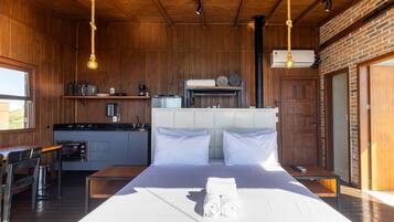 Een compacte hotelkamer met kitchenette, een bed met witte lakens en uitzicht op de omgeving.